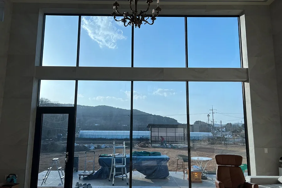 샹들리에가 달린 거실에서 모서리 통유리 너머로 산과 마당이 보이는 사진