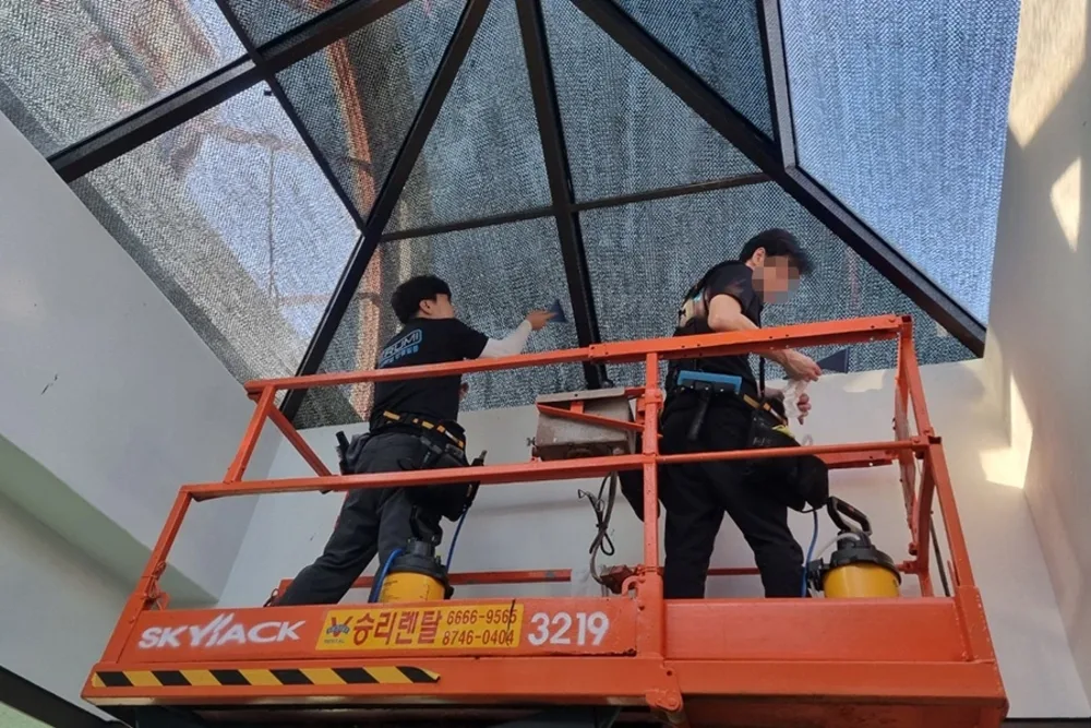 천장 채광창 안쪽에서 고소작업대로 필름을 부착하는 사진