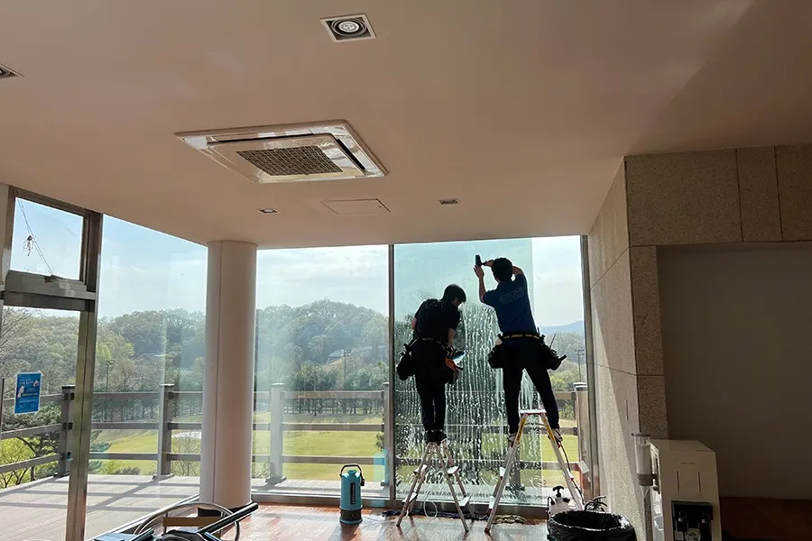 사다리 위에서 두 명의 작업자가 유리벽을 시공하는 사진