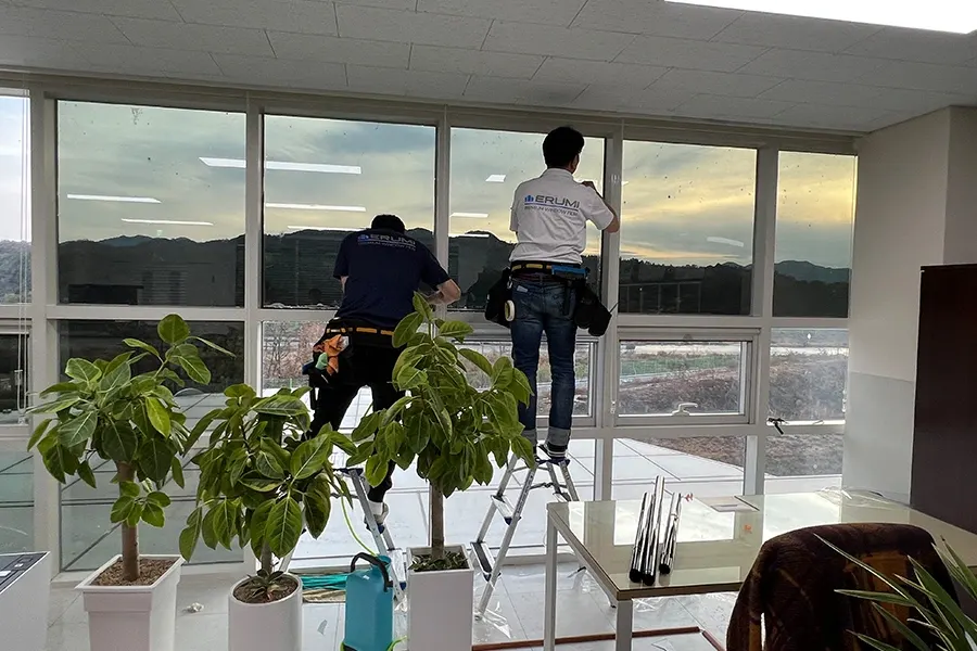 사다리 위에서 대형 통유리에 필름을 시공하는 작업자 사진