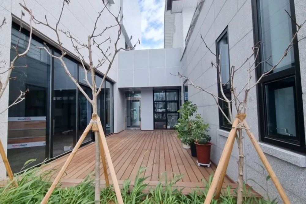 유리로 둘러싸인 건물 사이 목재 데크 정원 사진