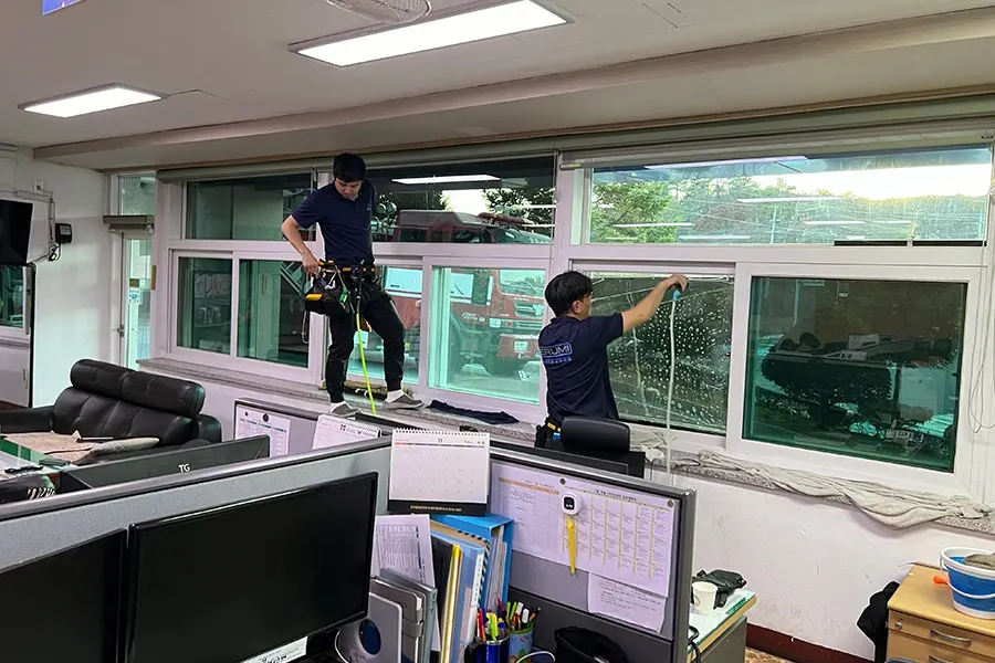 안전벨트를 착용하고 사무실 창문에 필름을 시공하는 작업자 사진