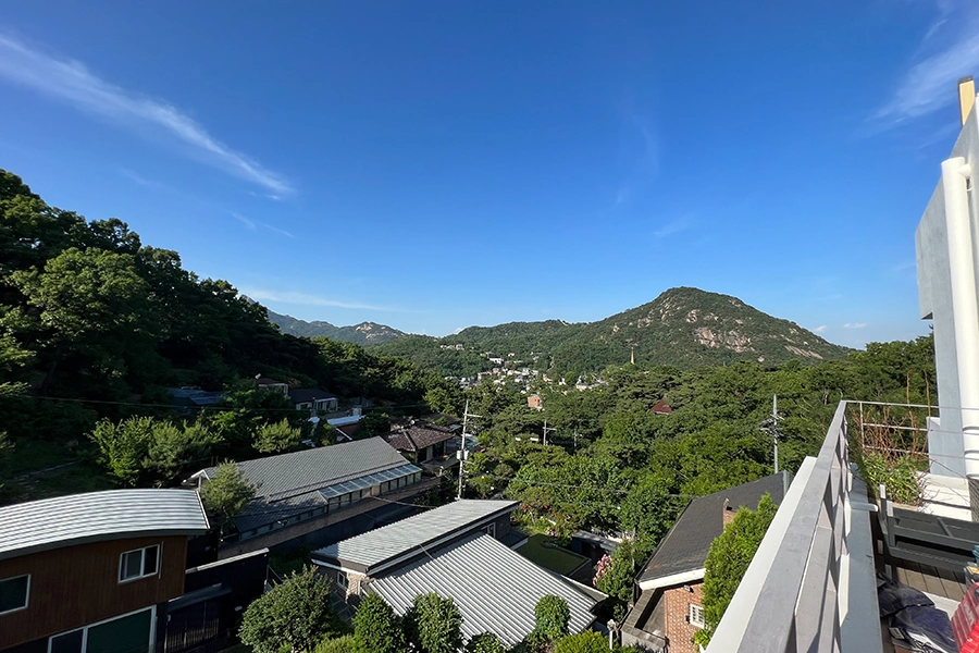 단독주택 옥상 데크 유리 썬룸 안에서 산과 이웃집 지붕이 보이는 사진